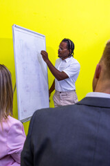 A latin man is writing on a white board in front of a group of people