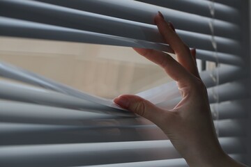 Woman separating slats of white blinds indoors, closeup
