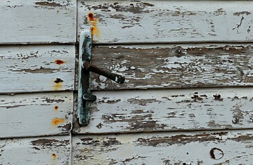 Door handle on an old wooden door covered with white koaska flying away from old age