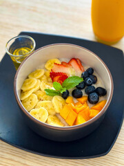 A colorful bowl of sliced bananas, strawberries, mango, and blueberries, served with honey and orange juice on the side