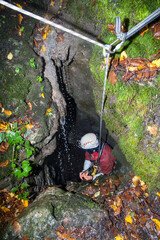  A speleologist man exploring a huge hidden cave hanging on a rope for safety and preparing to go...