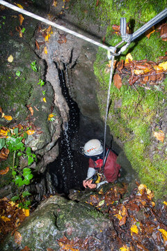  A speleologist man exploring a huge hidden cave hanging on a rope for safety and preparing to go down into the cave