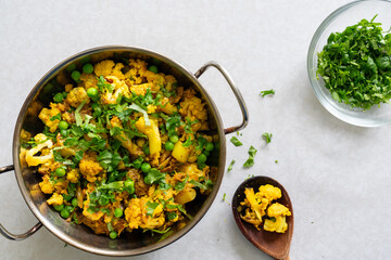 Freshly homemade spicy green pea and cauliflower curry, garnished with coriander in a wok, isolated on white background. Matar gobhi sabzi a traditional North Indian dish. View from above.