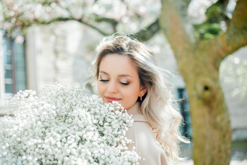 Beautiful young blonde with bouquet of flowers. Portrait of young woman near blooming magnolia in...