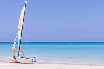 The beautiful beach front of the Cuban beach at Varadero in Cuba showing a catamaran sail boat on the sand with clean ocean waters and blue sunny skies in the summer time.