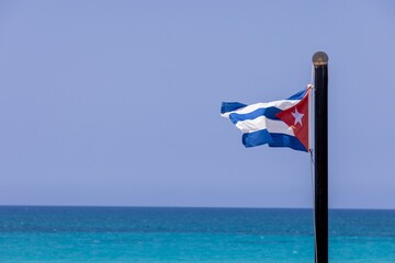 A Cuban flag blowing in the wind in the town of Varadero in Cuba with clear blue Skys and clean...