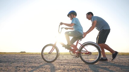 family play in the park. father teaching son to ride a bike. happy family kid dream concept. son learn to ride a bike silhouette. father supporting child son riding bike summer sunset in the park