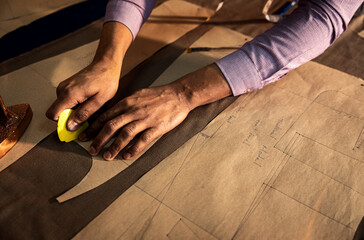 Close up of male fashion tailor hand working on the measurements for the suit design in his workshop.