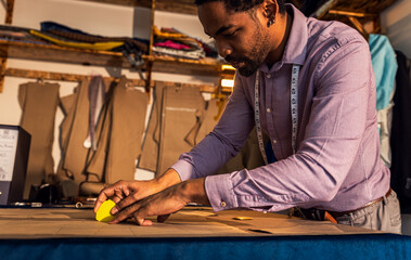 Male fashion tailor working on the measurements for the suit design in his workshop.