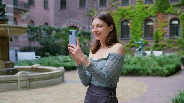 Portrait of beautiful young woman female standing outdoor holding mobile phone in hand and talking on online video call, content. Attractive girl communicating with friend using smartphone