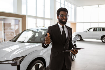 Young successful manager on background of rows of new car dealership crossovers. Portrait of...