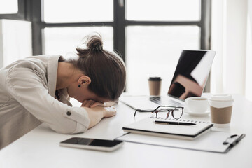 Tired and overworked business woman. Young exhausted girl sleeping on table during her work using laptop, digital tablet and smartphone. Entrepreneur, freelance worker or student in stress concept - 786193060