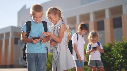 children group school children look at the smartphone video. school learning kid concept. group of kids with backpacks lifestyle playing smartphone near the school building outdoors