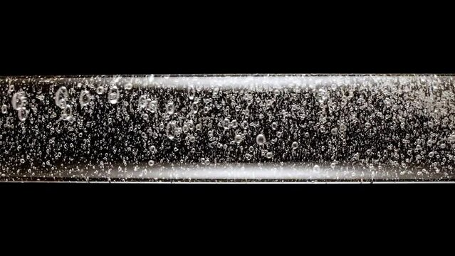 Macro shot of fine air bubbles rising in water in glass test tube on black background. Effervescent tablet aspirin. The medicine concept, health care, treatment. Slow motion. High quality FullHD 