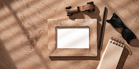 Overhead view of creative setting featuring wooden picture frame without image, alongside notepad, pair of black sunglasses, and black pencil. Father's Day concept
