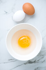 Fresh uncooked goose egg in a bowl and raw chicken eggs on a white marble background, above view, vertical shot
