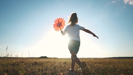 kid run pinwheel. little baby girl silhouette play with windmill toy wind in the park. happy family...