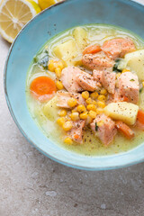 Chowder with salmon served in a turquoise bowl, vertical shot on a beige stone background, middle closeup
