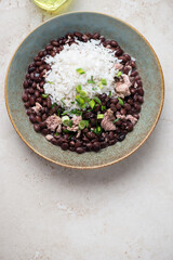 Rustic plate with black beans and white rice on a light-beige stone background, vertical shot with space, above view