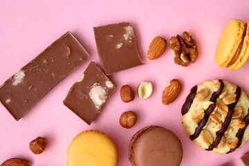 Pastel macarons, almond chocolate, peanut butter cookies and various nuts on bright pink background. Top view.