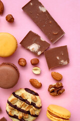 Pastel macarons, almond chocolate, peanut butter cookies and various nuts on bright pink background. Top view.