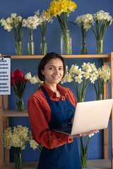 Portrait of a female florist flower shop owner using a laptop in her store. Small business
