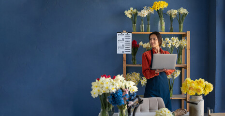 Female florist using laptop looking at space for text working in her flower shop. concept of small business and flower delivery. Banner