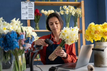 Florist concept. Beautiful hispanic woman entrepreneur working at own flower shop making bouquet. Female makes bunch of flowers in her store.