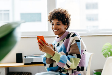 Freelancer in colorful sweater using smartphone in office - obrazy, fototapety, plakaty