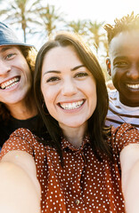 Vertical photo group of happy multiracial people taking a selfie with mobile phone outdoors with back sunlight. Multiethnic friends having fun on summer vacation.