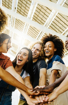 Vertical photo of multiracial happy friends with hands in stack. Multi-ethnic diverse group of college students joining their hands. Stacking hand concept, community, unity and teamwork concept