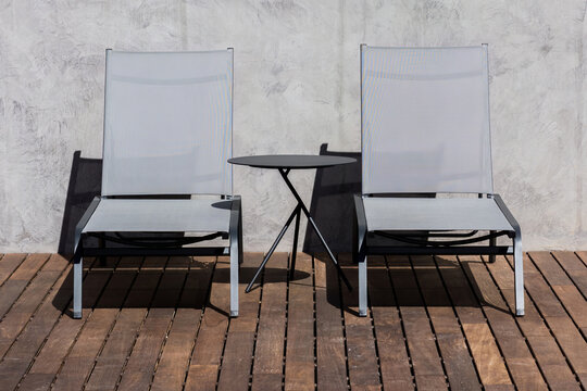 Two Modern Lounge Chairs and a Side Table on a Wooden Deck Under Sunlight