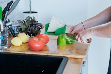 Woman chopping vegetables on bamboo cutting board, a preparation step in a fresh and healthy home-cooked meal.