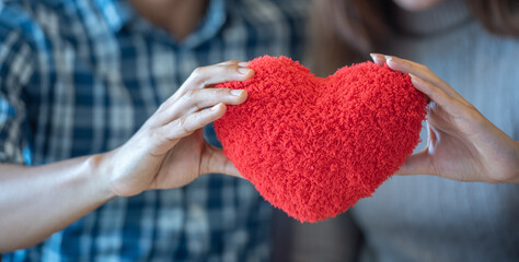 Lover couple happy in love relaxing on sofa looking in eye smiling teasing with big red heart shape...