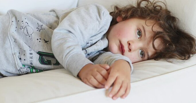 Young boy resting on a white sofa, looking unwell and tired