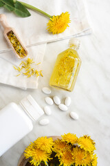 Flat lay composition with essential oil, vitamins and dandelion flowers on white marble table. Flower essential oil. Herbal medicine. Top view.