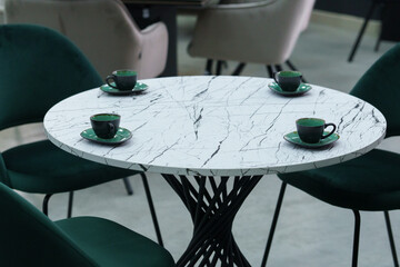 White wooden table complete with green wooden chairs with soft fabric upholstery. Green cups on the table