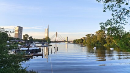 A large city with high-rise buildings and parks stands on the banks of the river. A bridge on...