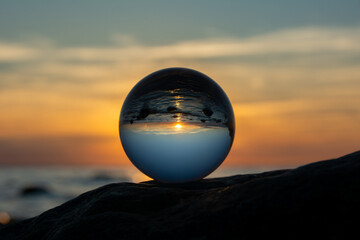 Ball made of glass lies on a stone in which the beach and the sea are reflected - 786218665