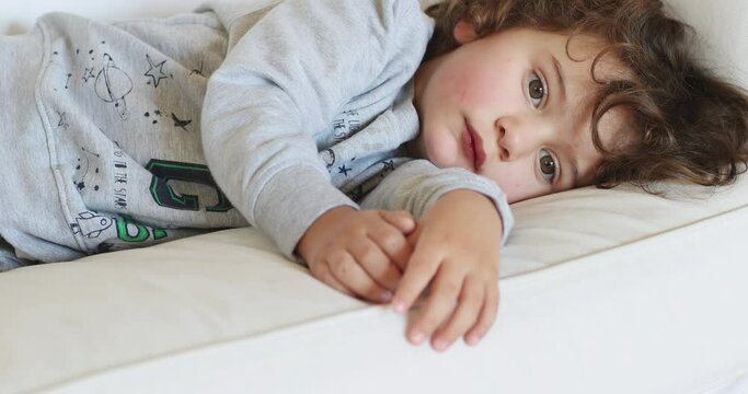 Young boy resting on a white sofa, looking unwell and tired