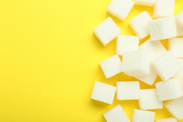 Fototapeta na wymiar White sugar cubes on yellow background, top view. Space for text
