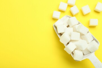 White sugar cubes and scoop on yellow background, top view. Space for text