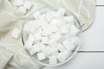 Fototapeta na wymiar Many sugar cubes in glass bowl on white wooden table, top view