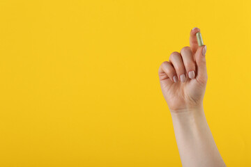 Woman holding vitamin capsule on yellow background, closeup with space for text. Health supplement
