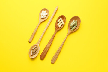 Different vitamin pills in spoons on yellow background, flat lay