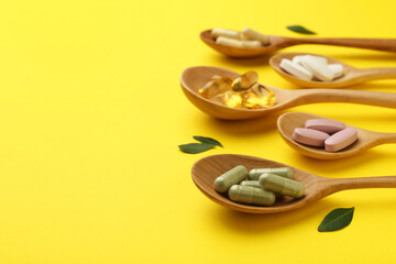 Different vitamin pills in spoons and green leaves on yellow background, closeup. Space for text