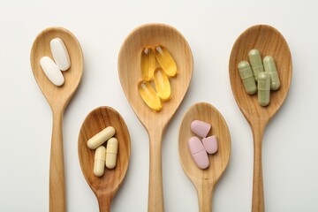 Vitamin capsules in wooden spoons on white background, flat lay