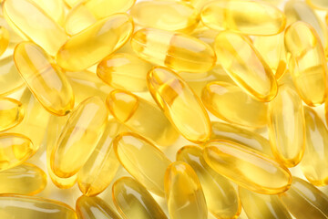 Yellow vitamin capsules as background, top view