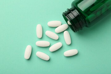 Vitamin pills and bottle on mint color background, top view
