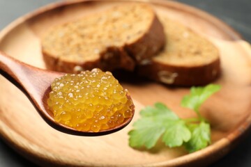 Fresh pike caviar in spoon, bread and parsley on table, closeup